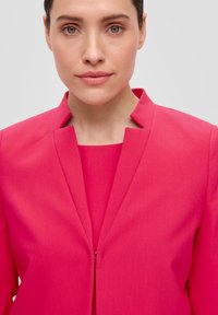 Fuchsia blazer met een mandarin kraag, strakke lijnen en een verborgen ritsdetail, gecombineerd met een bijpassende fuchsia top eronder.