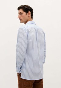 Camisa de manga larga a rayas azul claro, confeccionada en una tela suave, con líneas verticales, puños abotonados y un cuello clásico.