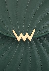 Zelená kožená kabelka s prošívaným designem. Obsahuje zlaté kovové detaily ve zigzagovém tvaru a kontrastní tmavší stehy.