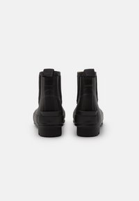Bottines noires à chevilles avec une finition en caoutchouc lisse, des panneaux latéraux élastiques et une semelle texturée ; elles se caractérisent par un design minimaliste et aucune quincaillerie visible.