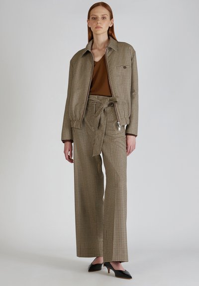 Bruin geruit jasje met bijpassende wijde broek, met een strakke taille en een bruine top eronder. Zwarte spitse hakken maken de look compleet.