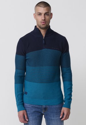Suéter de punto con cremallera que presenta un degradado de azul oscuro a verde azulado, con detalles a rayas y puños y dobladillo acanalados.