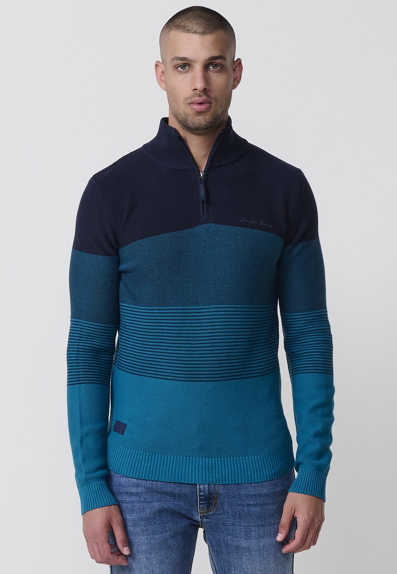 Pleteni zip-up pulover z gradientom temno modre do svetlo teal barve, z črtastimi detajli in rebrastimi manšetami ter robom.