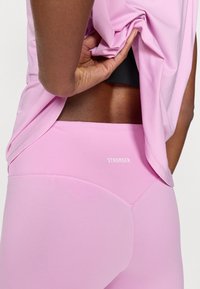 Ροζ αθλητικό κολάν με αντίθετη μέση, που φέρει τη λέξη «STRONGER» σε λευκό. Το τοπ είναι ανοιχτό ροζ και άνετο.