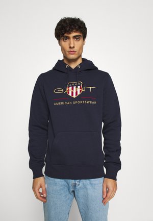 Felpa con cappuccio blu navy realizzata in misto cotone, dotata di tasca frontale, cappuccio con cordini e logo ricamato con dettagli rossi e dorati.