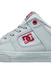 Lys grå sneakers med en tekstureret overflade, rød logo, grå snørebånd og syninger, med en gummisål og cirkulære øjer.
