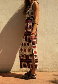 Hæklede maxi kjole i rig maroon og beige med geometriske mønstre og sideslids; parret med sorte sandaler med dekorative stropper.