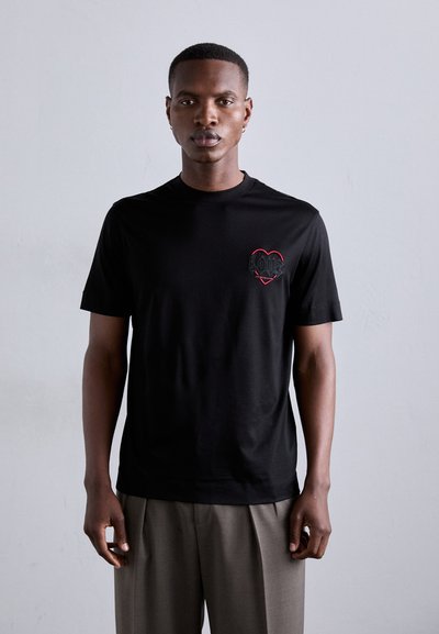 T-shirt noir à manches courtes avec un design de cœur brodé rouge portant le mot "AMOUR". Le tissu semble lisse et léger.