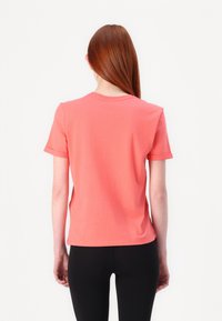 Korallfarget t-skjorte med korte ermer laget av bomull, med rund hals, rett snitt og oppbrettede ermeender, kombinert med svarte leggings.