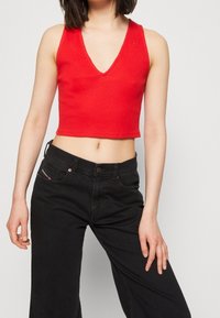 Haut court en rouge à côtes avec un décolleté en V profond, porté avec un pantalon noir. Le tissu semble doux et décontracté.