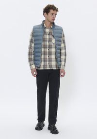 Doudoune grise matelassée sur une chemise à carreaux beige et marine, associée à un pantalon noir et des bottes noires à lacets.