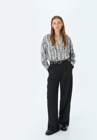 Blusa de manga larga, estampada con print de serpiente en blanco y negro, combinada con pantalones negros de pierna ancha y cintura alta, y un cinturón negro.