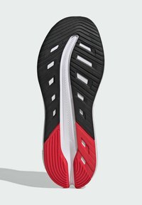 Semelle de chaussure de sport avec un design noir et rouge, ornée de rainures texturées, d'accents blancs et de sections découpées pour une meilleure traction et flexibilité.
