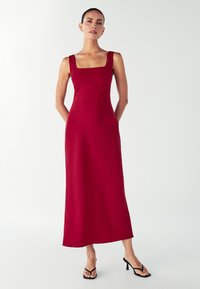 Červené maxi šaty bez rukávov so štvorcovým výstrihom, priliehavým korzetom a splývavou sukňou. Hladká tkanina s jemným leskom.