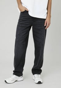 Jean en denim foncé avec une coupe droite, présentant des détails de couture subtils et une texture lisse. Porté avec un t-shirt oversize blanc et des baskets blanches.