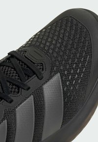 Μαύρο αθλητικό παπούτσι με επάνω μέρος από δίχτυ και υφές, επίπεδα κορδόνια και τρεις σκοτεινές γκρι ρίγες στο πλάι.