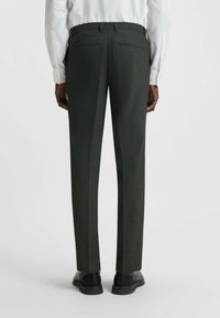 Dunkelgrüne, maßgeschneiderte Hose aus strukturiertem Stoff, mit geraden Beinen und klassischer Passform. Verfügt über Gesäßtaschen und einen Bund. Schwarze Schuhe.