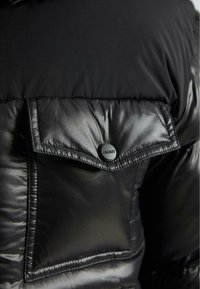 Čierna prešívaná bunda s vreckom na klopu zabezpečeným okrúhlym matným čiernym gombíkom s vyrazeným logom "JACKIT".