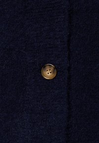 Marine wol stof met een zachte textuur, versierd met een ronde gouden knoop met vier gaten, genaaid aan de linkerkant van een kledingstuk.