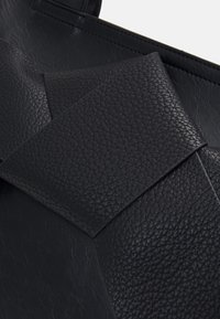 Svart texturerad läderhandväska med en stor vikflik som detalj. Ytan har en pebblad finish med släta accenter.