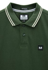 Polo verde con strisce doppie bianche sul colletto, due bottoni neri e etichetta del marchio "Weekend Offender" sul petto e all'interno del colletto.