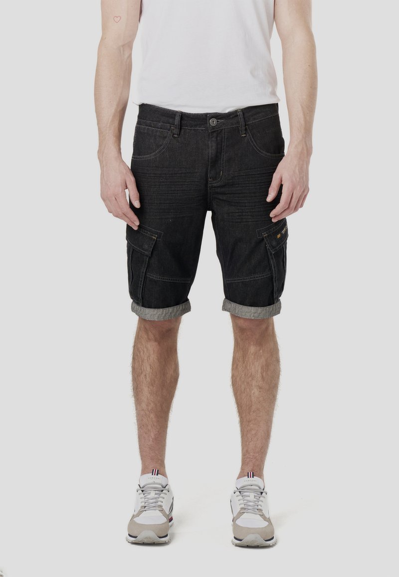 Shorts cargo en denim foncé avec revers retroussés, présentant de multiples poches et des lignes de texture subtiles. Portés avec un t-shirt blanc uni et des baskets.