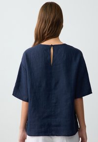 Camicia di lino blu navy con maniche corte, caratterizzata da un dettaglio a chiave sulla schiena e una vestibilità rilassata. Tessuto liscio con cuciture minime.