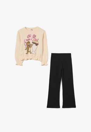 Beige longsleeve shirt met een cartoonafbeelding van een muis en een ijsje; gecombineerd met zwarte flared broek met elastische tailleband.