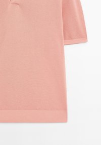 Ljusrosa polo skjorta gjord av texturerad stickad tyg, med en klassisk krage och korta ärmar. Bottom nederkant är ribbad.