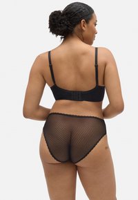 Sujetador negro con tirantes ajustables y espalda de malla; combinado con bragas negras de red con bordes ondulados. Textura suave en general.