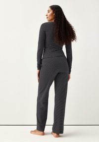 Svartvitrandigt pyjamaset med långärmad, figurnära topp och lösa byxor, tillverkat av mjukt, stretchigt tyg med en slät textur.