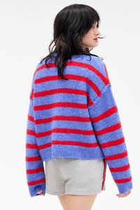 Πλεκτό πουλόβερ σε ανοιχτό μπλε με κόκκινες ρίγες, κοντή σχεδίαση, μακριά μανίκια και απαλή, φουντωτή υφή. Φορεμένο με γκρίζες σορτς.