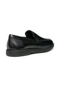 Mocassin noir en cuir à enfiler avec un petit talon, bout rond et semelle lisse, présenté de l'extérieur sur un fond blanc.