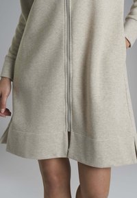 Abito grigio chiaro con zip, realizzato in tessuto morbido, dotato di maniche lunghe e spacco laterale all'orlo per facilitare i movimenti.