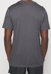 Szara bawełniana koszulka z krótkimi rękawami, okrągłym dekoltem i gładką fakturą. Widoczne przeszycia wokół krawędzi dołu i rękawów.