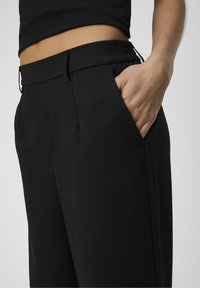 Zwarte broeken met een vlakke voorkant, zijzakken en een gladde textuur. De band heeft elastische elementen voor flexibiliteit.