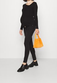 Svart långärmad topp, mörka skinny jeans, svarta klackskor och en orange mockaväska. Outfitten har avslappnade, figurnära designer.