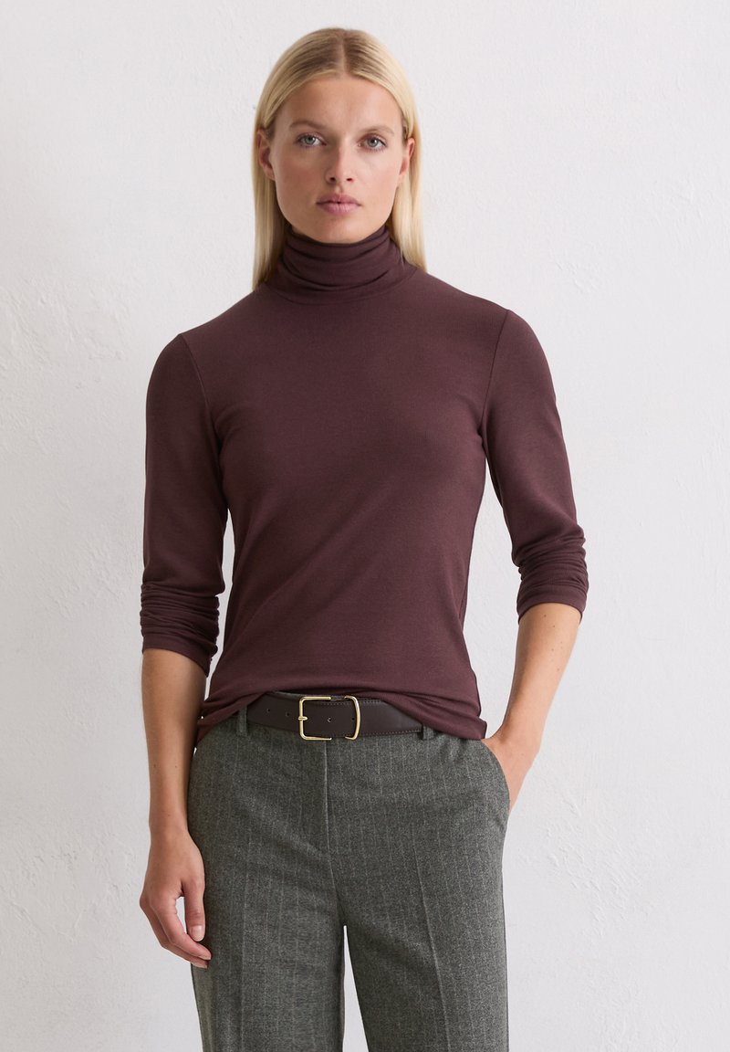 Bordeauxfarbenes Rollkragenoberteil mit langen Ärmeln, figurbetontem Schnitt und glatter Textur. Kombiniert mit grauen, gestreiften trousers und einem braunen Gürtel mit goldener Schnalle.