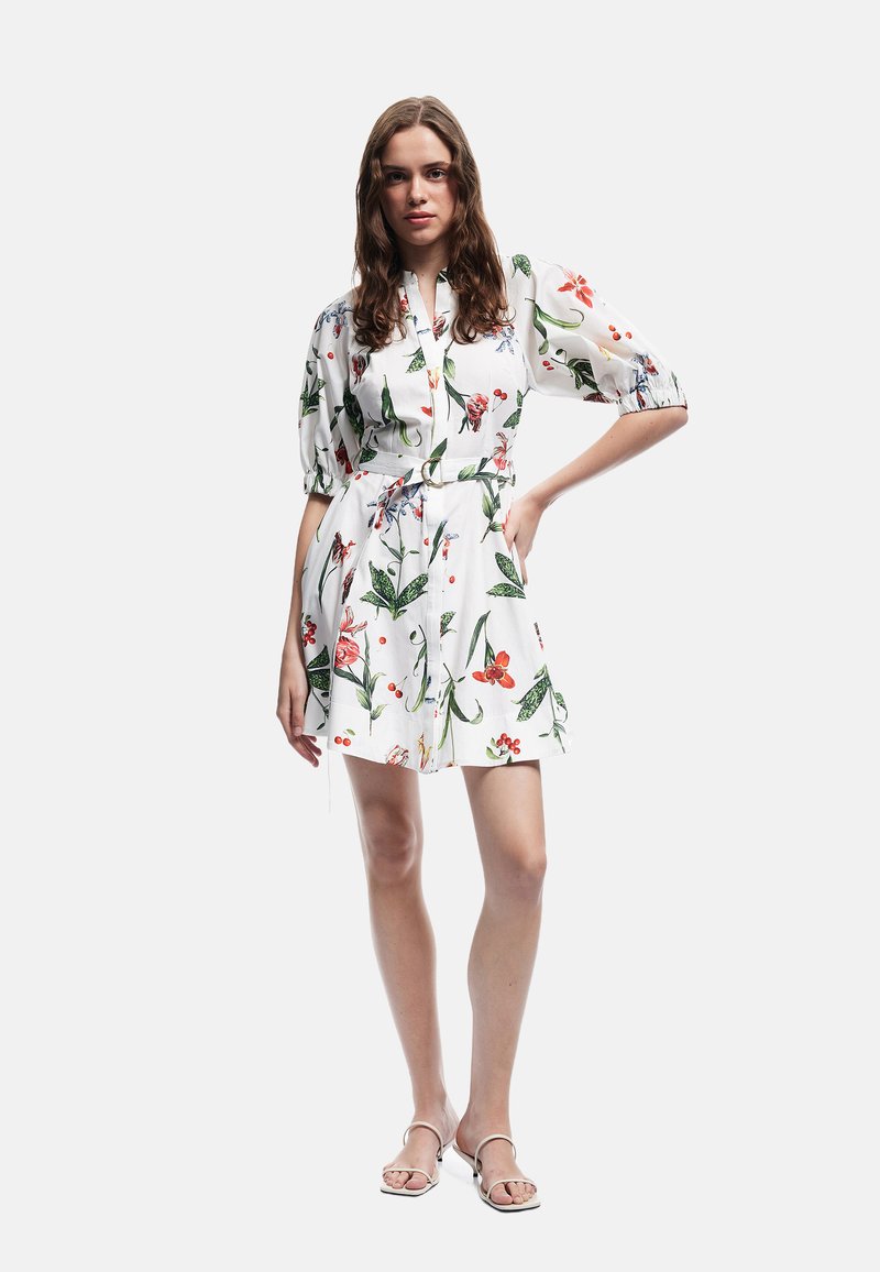 Bloemen shirtjurk van witte stof met kleurrijke patronen van bloemen en bladeren, met poffende mouwen en een tailleband.