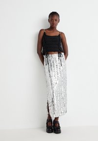 Haut court en tricot noir avec des liens ajustables, associé à une jupe maxi en sequins argentés avec des fentes sur les côtés. Des chaussures à plateforme noires complètent le look.