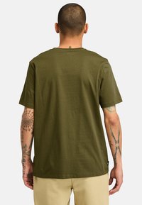 Olivově zelené tričko s krátkým rukávem vyrobené z bavlny, s kulatým výstřihem a bočním štítkem, s hladkým povrchem a uvolněným střihem.
