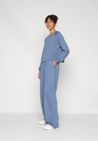 Conjunto de loungewear de tela suave y azul que incluye un sudadera recortada y un pantalón suelto con bolsillos laterales y detalles de botones en el dobladillo.