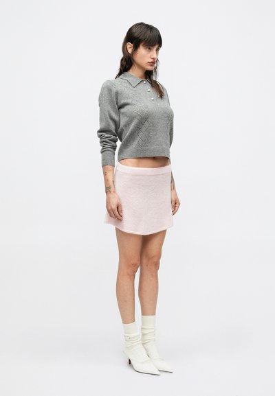 Sivý pletený sveter s golierom a vzorom kosoštvorcov, skombinovaný s svetloružovou mini sukňou. Modelka má na sebe biele členkové topánky a ponožky.