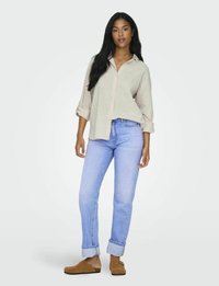 Lätt beige knappar-up skjorta med uppvikta ärmar, kombinerad med ljusblå raka jeans och bruna slipskor.