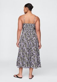 Maxikleid mit Blumenmuster und dünnen Trägern, mit gerafftem Rücken, in Lila- und Schwarztönen, aus fließendem, leichtem Stoff. Akzentuiert durch ein gemustertes Design.