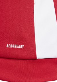 Roter sportlicher Stoff mit strukturiertem Strick, einem glatten weißen Einsatz und dem Logo "AEROREADY" in weißem Text.