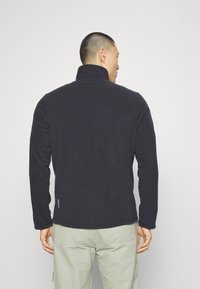 Schwarze Fleecejacke mit hohem Kragen und langen Ärmeln, mit einer glatten Textur und einem seitlichen Reißverschlussfach.