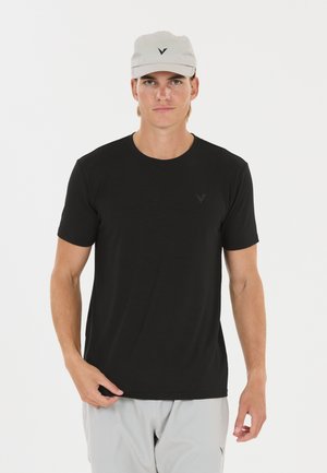 Homme portant un t-shirt noir, un short gris clair et une casquette gris clair avec un petit logo noir sur chaque article.