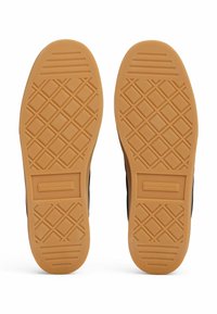 Suelas de goma con un patrón texturizado en forma de diamante; color beige con el logo de la marca. Bordes lisos y lados negros contrastantes.