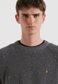 Maglione grigio lavorato a maglia con collo a coste, motivo testurizzato e sottili punti riflettenti. Presenta un piccolo logo arancione sul petto.